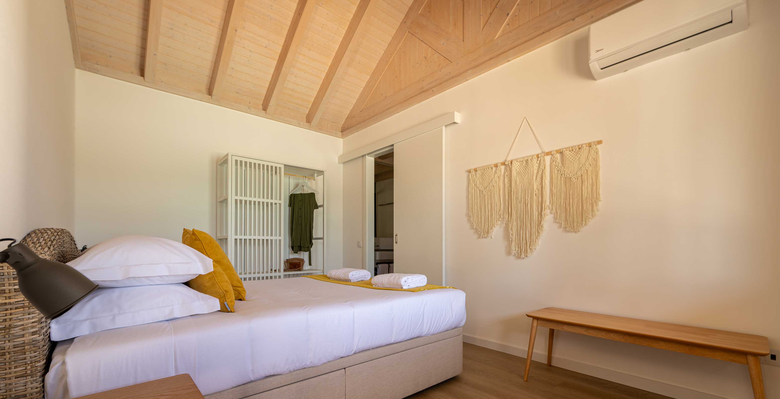A Standard Green Villa do Pestana Comporta Village Residences tem um quarto minimalista com uma cama e um banco