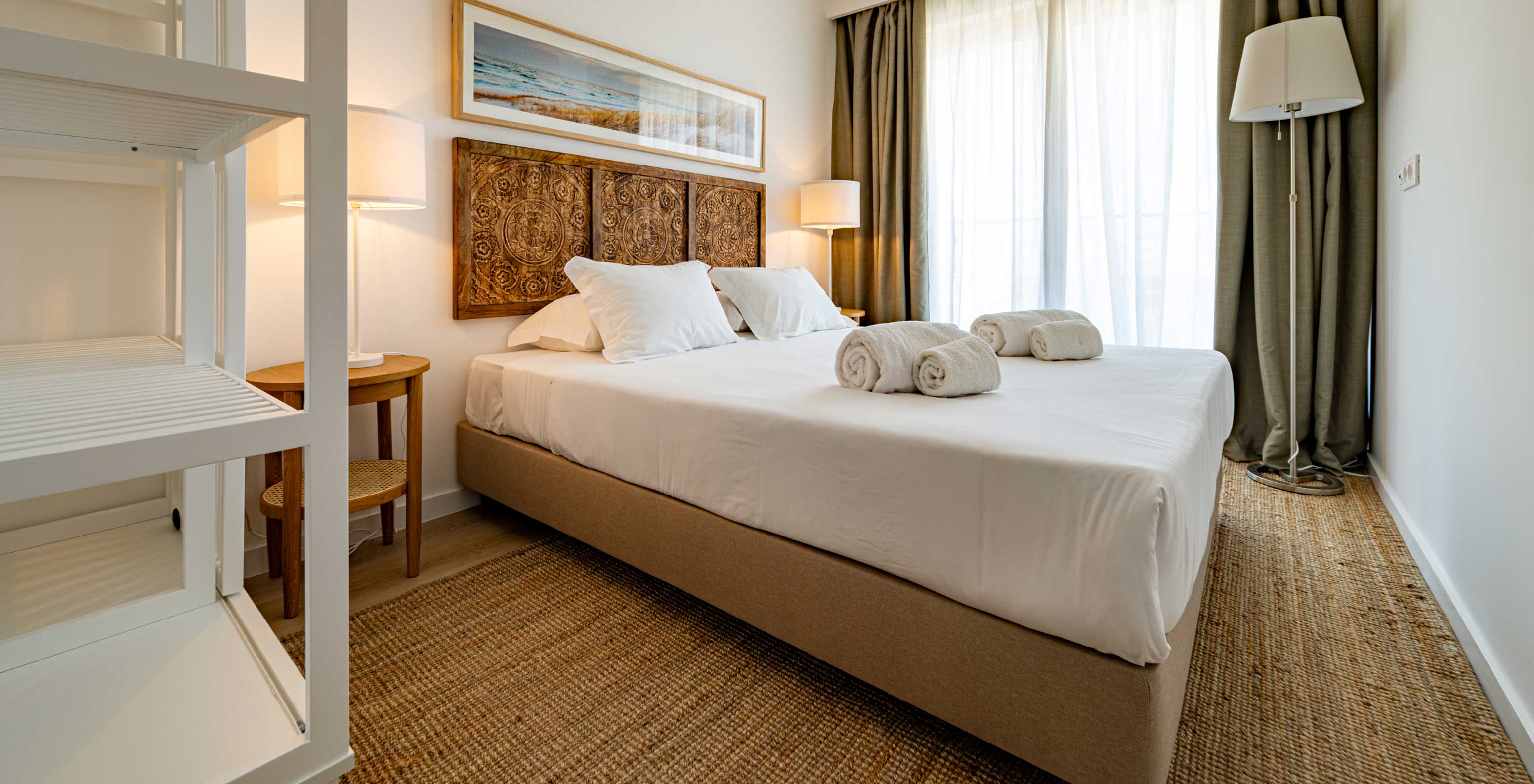 Quarto do Pestana Porto Covo Village com cama de casal, cabeceira em madeira esculpida e luz natural pelas cortinas