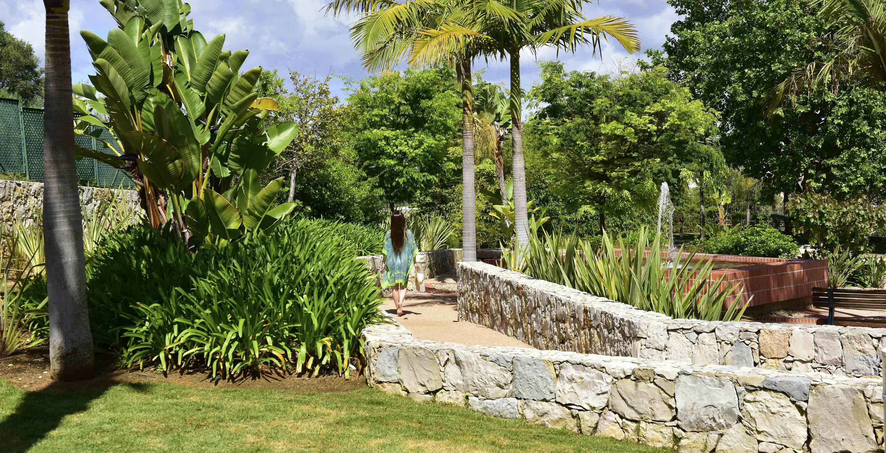 Hóspede a passear no jardim com vegetação tropical do Pestana Alvor Park, Aparthotel 4 Estrelas no Alvor com Piscina