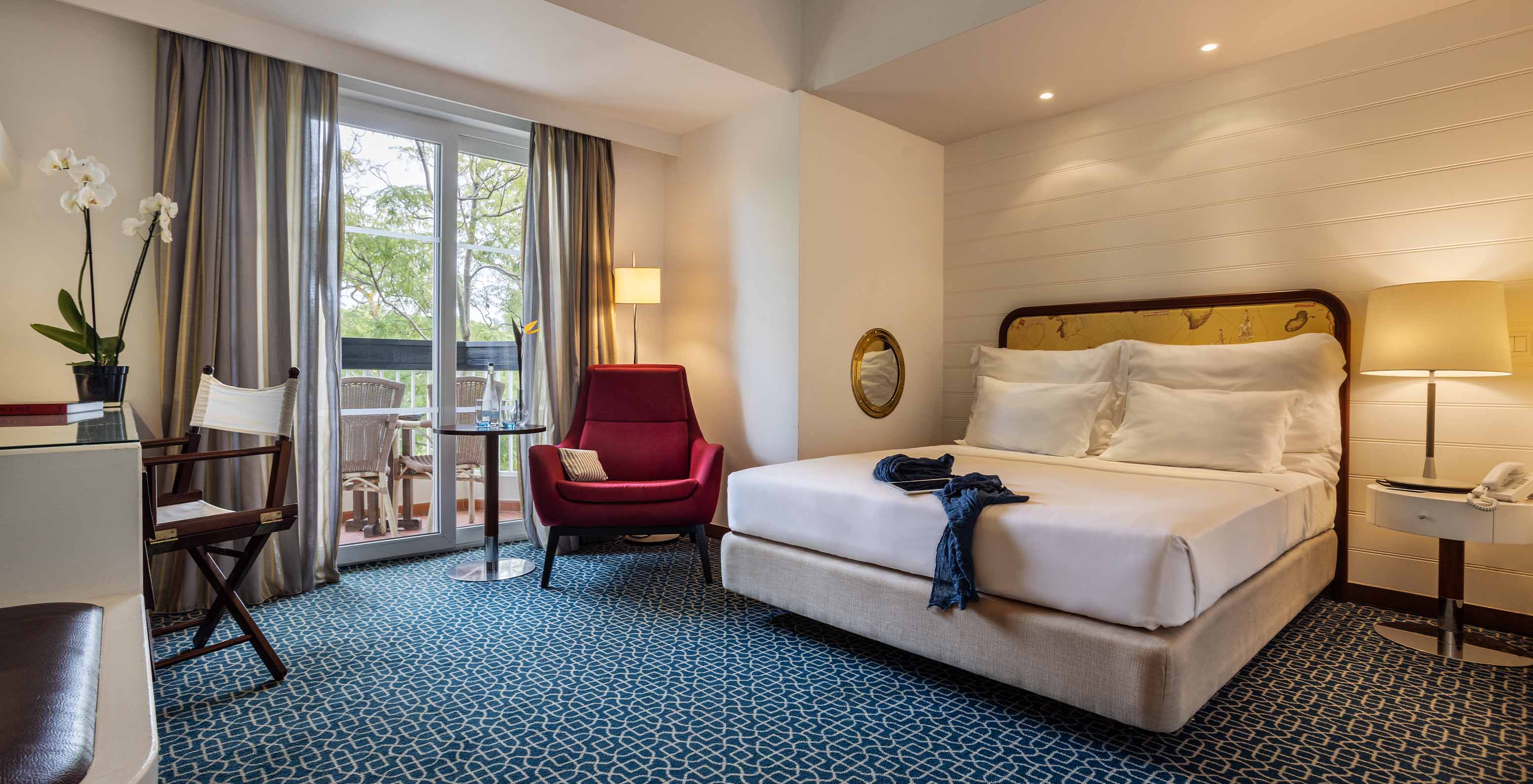 A Suite Vista Jardim do Pestana Alvor Praia tem cama de casal, cadeirão vermelho e varanda com vista jardim e cadeiras