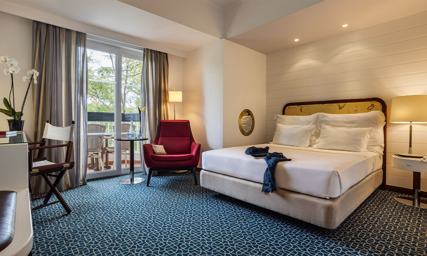 A Suite Vista Jardim do Pestana Alvor Praia tem cama de casal, cadeirão vermelho e varanda com vista jardim e cadeiras