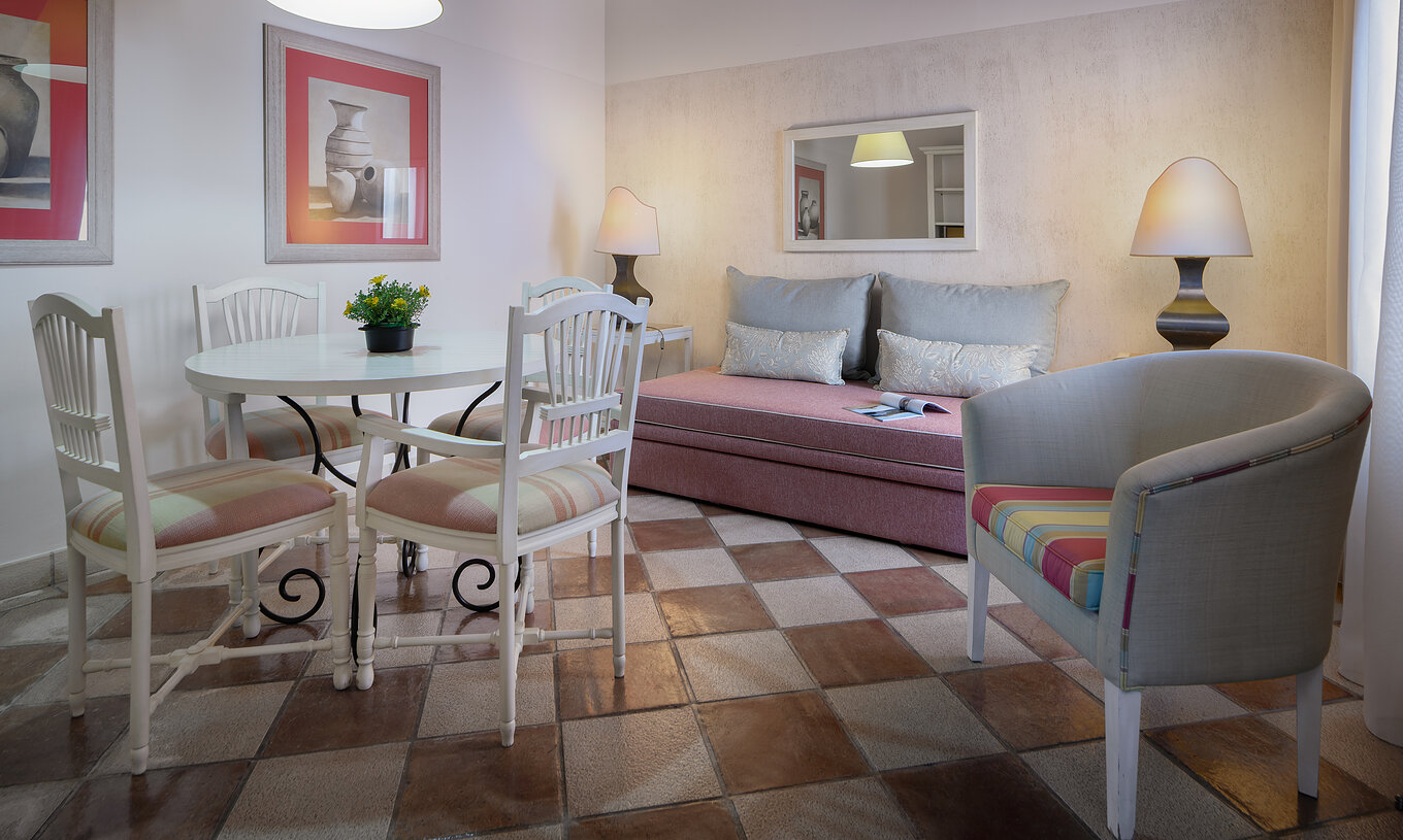 A Suite Jardim Resort do Pestana Vila Sol - Vilamoura tem uma sala com um sofá, uma mesa, cadeiras e um espelho na parede