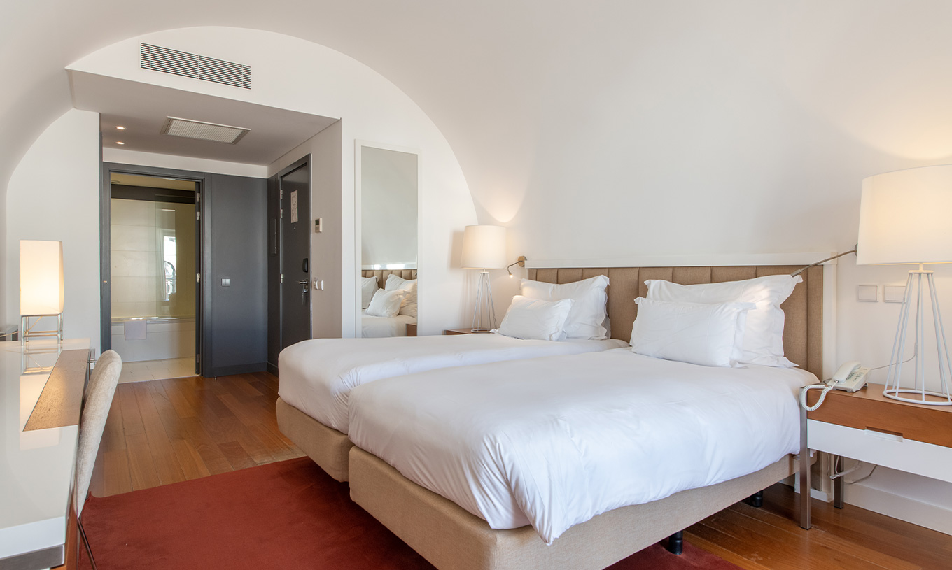 O Quarto Clássico do Pestana Cidadela Cascais tem duas camas individuais, um tapete vermelho e um espelho grande