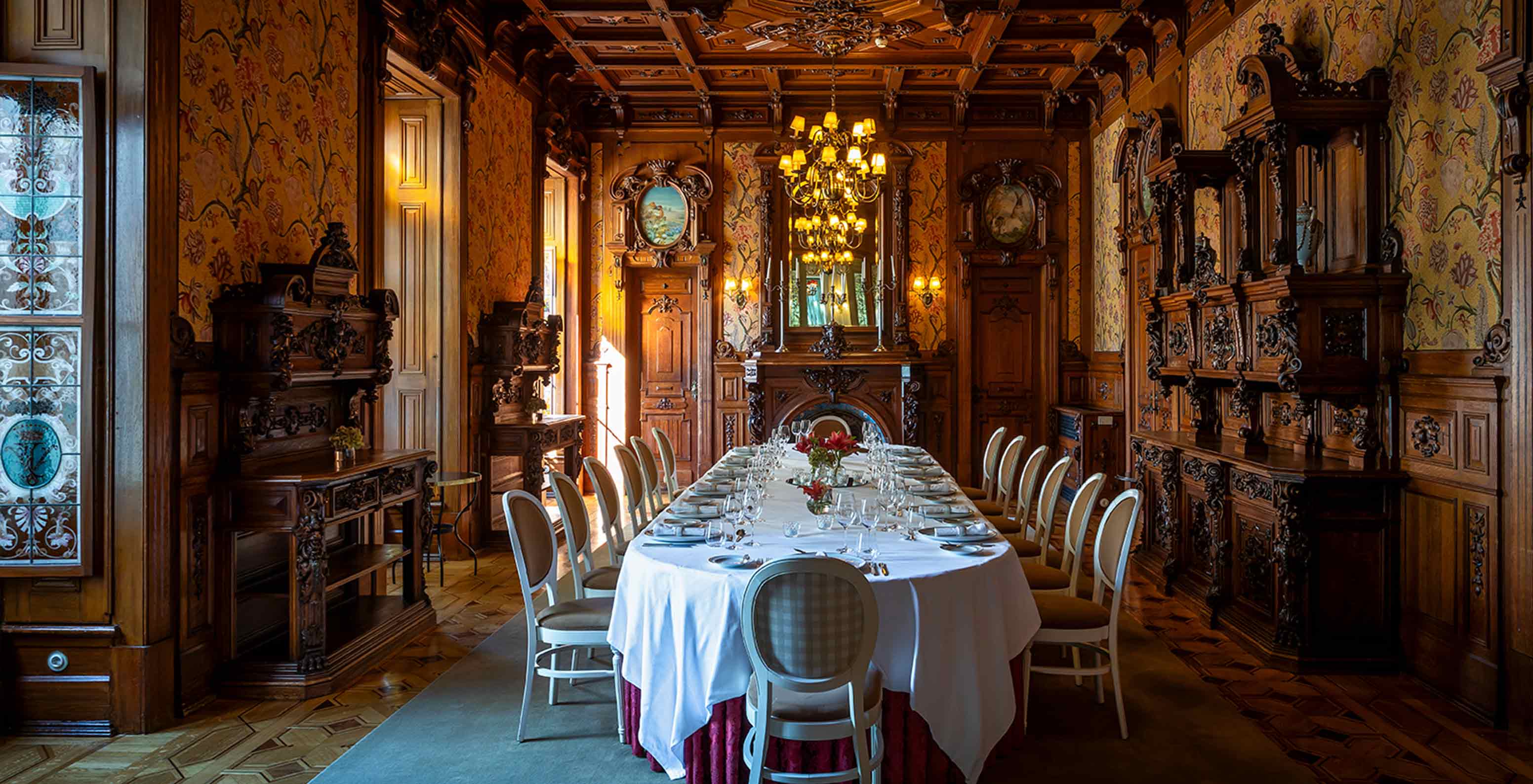 O Pestana Palace Lisboa tem uma sala de jantar privada com um teto em madeira com três candelabros e uma mesa oval