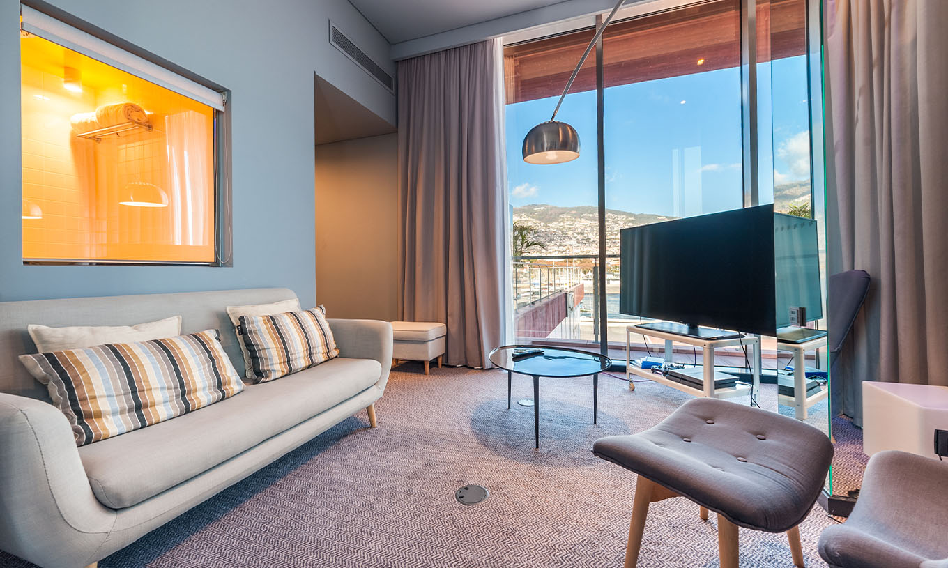 A CR7 Suite do Pestana CR7 Funchal tem uma sala de estar com um sofá, uma televisão e uma janela com vista para o Funchal