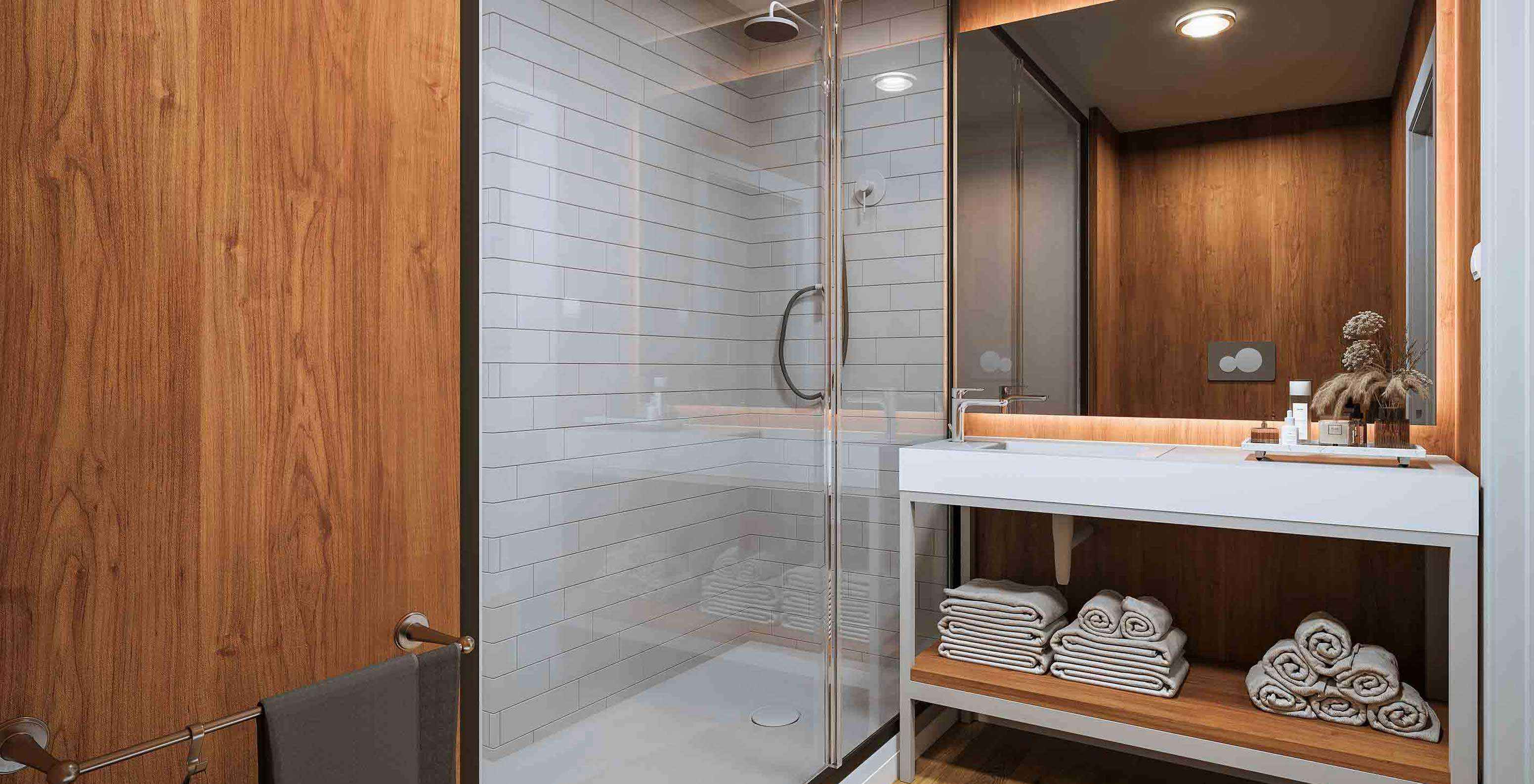 Casa de banho moderna com duche envidraçado, toalhas dobradas e espelho iluminado no Pestana Dunas Porto Santo