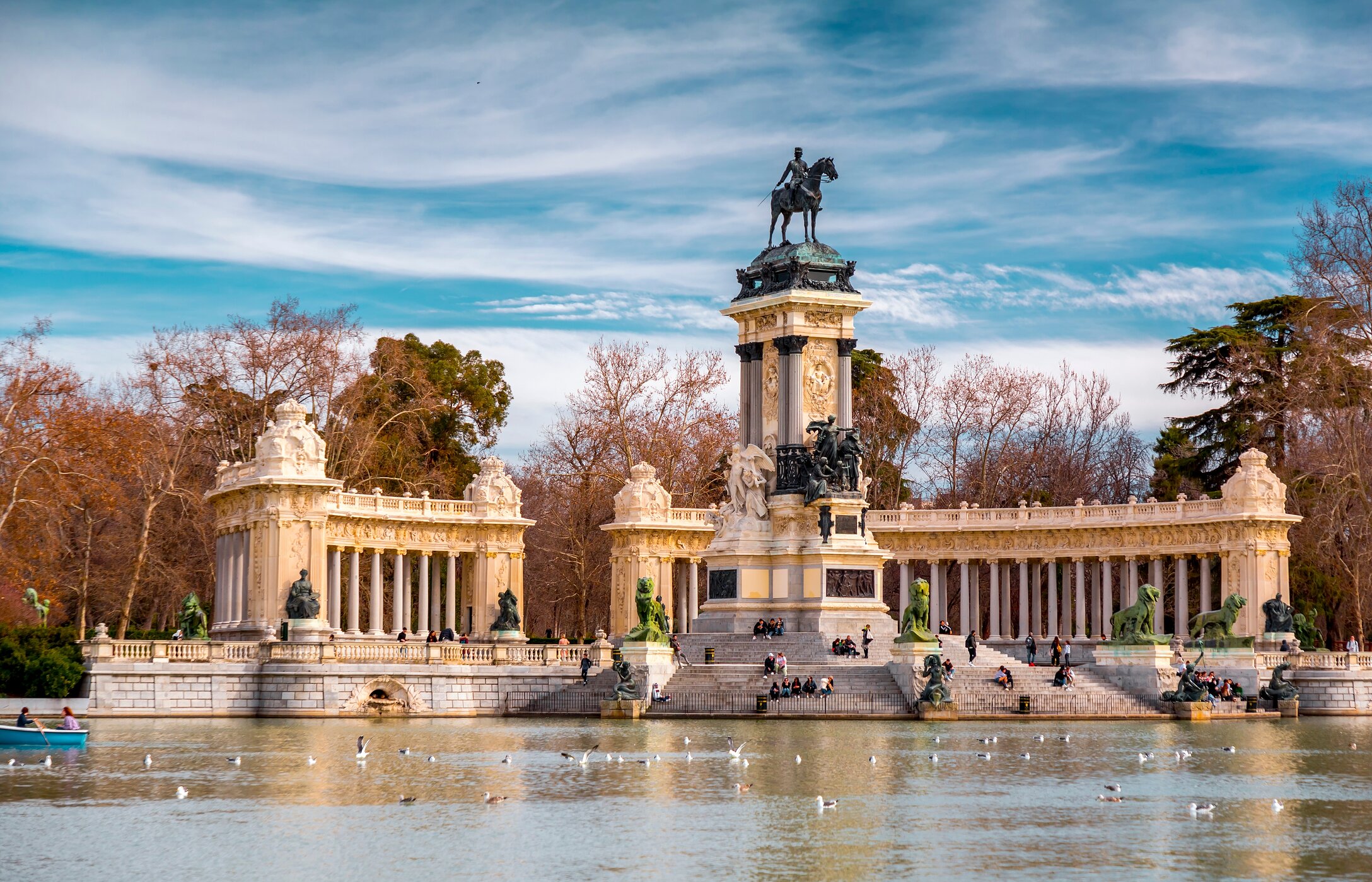 Lago do Parque do Retiro no centro de Madrid, com várias pessoas a descansar nas escadas e pássaros pousados no lago