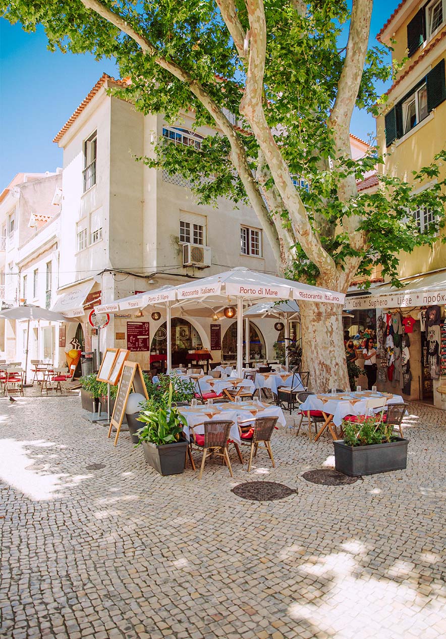 Freiluftrestaurant am Camões-Platz in Cascais, mit Tischen und Stühlen unter einem großen Baum an einem sonnigen Tag