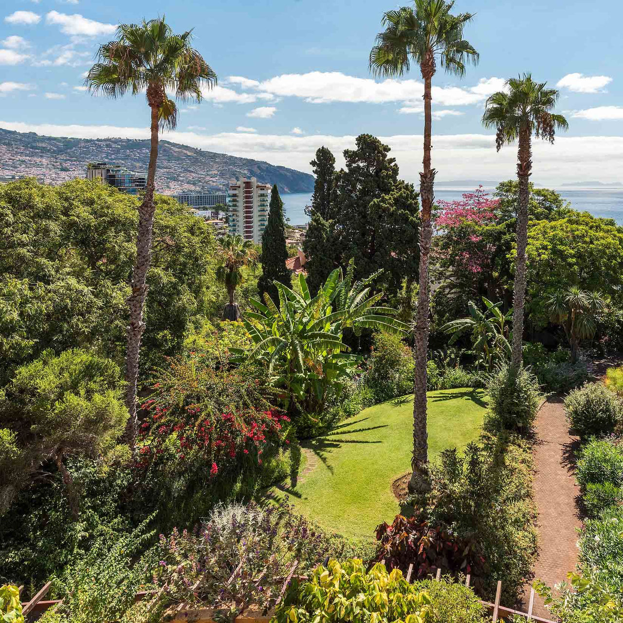 Garten mit tropischen Pflanzen, Meerblick und Hügel im Pestana Village, romantisches Hotel in Funchal, Madeira.