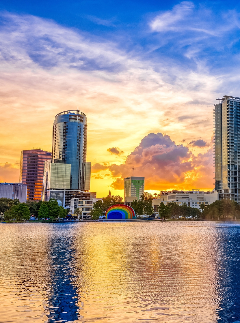 Stadtlandschaft von Orlando bei Sonnenuntergang, mit einem See und einem Springbrunnen im Vordergrund