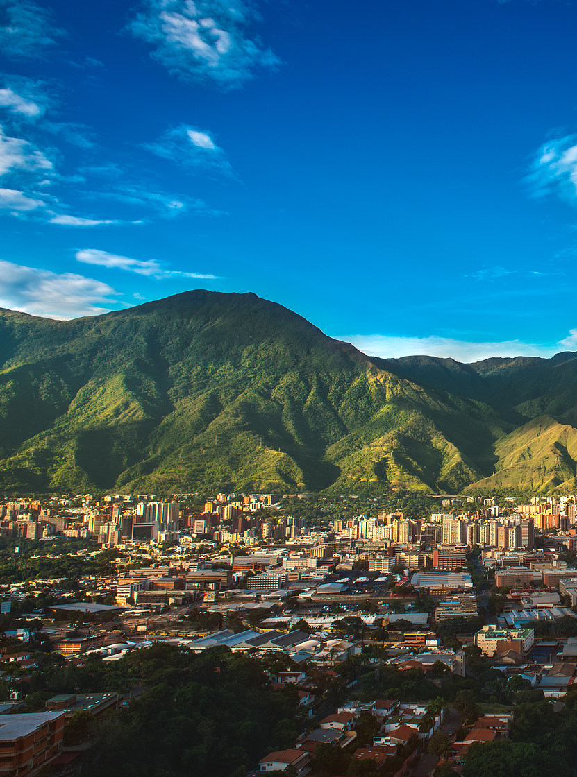 Luftaufnahme der Stadt Caracas mit hohen Gebäuden, die im Gegensatz zur bergigen Natur und dem blauen Himmel stehen