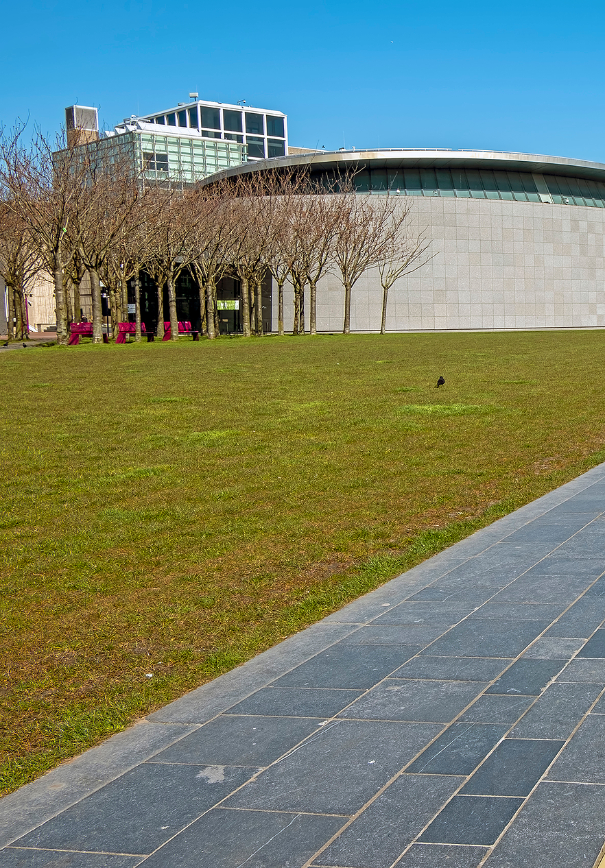 View of the grass and paved area of Museumplein in Amsterdam with aligned trees and the museum building in the background