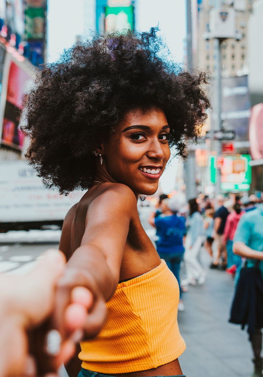 Mujer sonriente sosteniendo la mano de alguien en Times Square, con letreros brillantes y gente al fondo