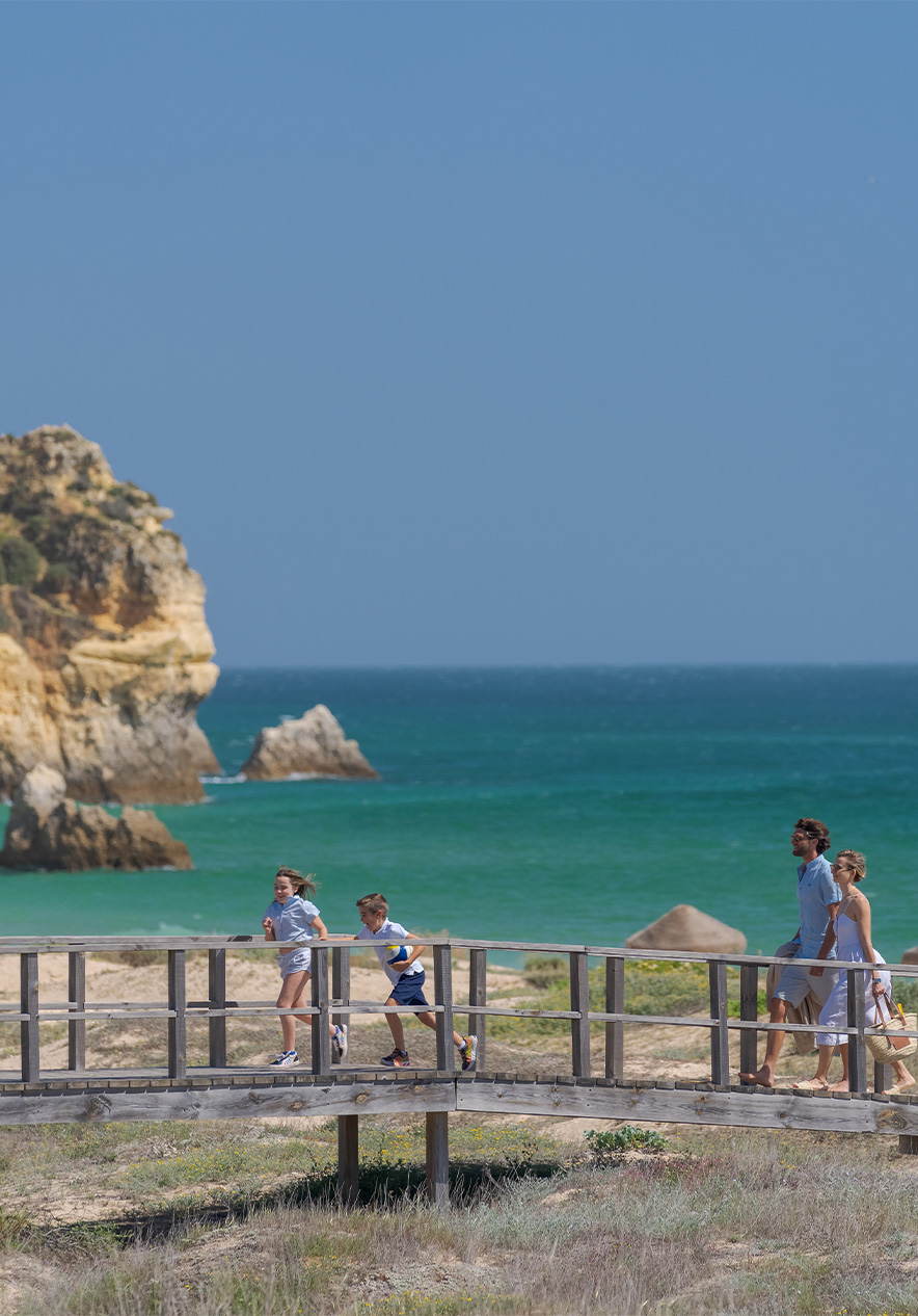 Pasadizos de madera de la playa de Alvor, con el mar de fondo y niños corriendo con sus padres