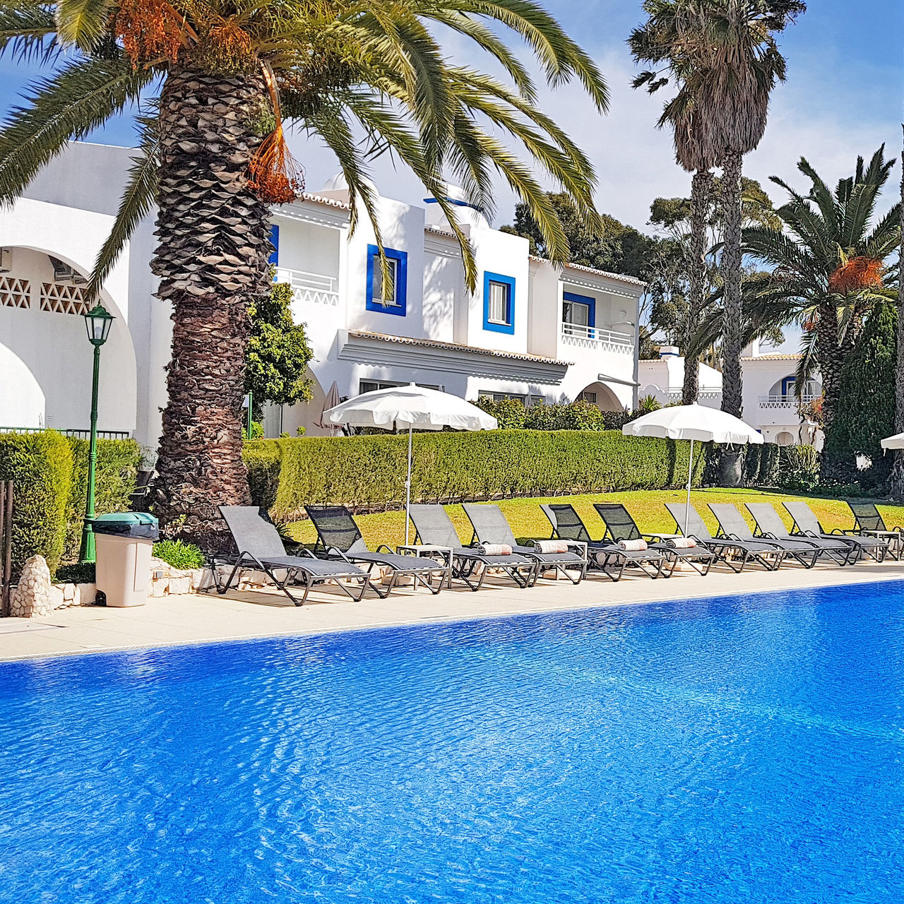 Buitenzwembad hotel Carvoeiro, met ligstoelen, parasols, palmbomen en villa's