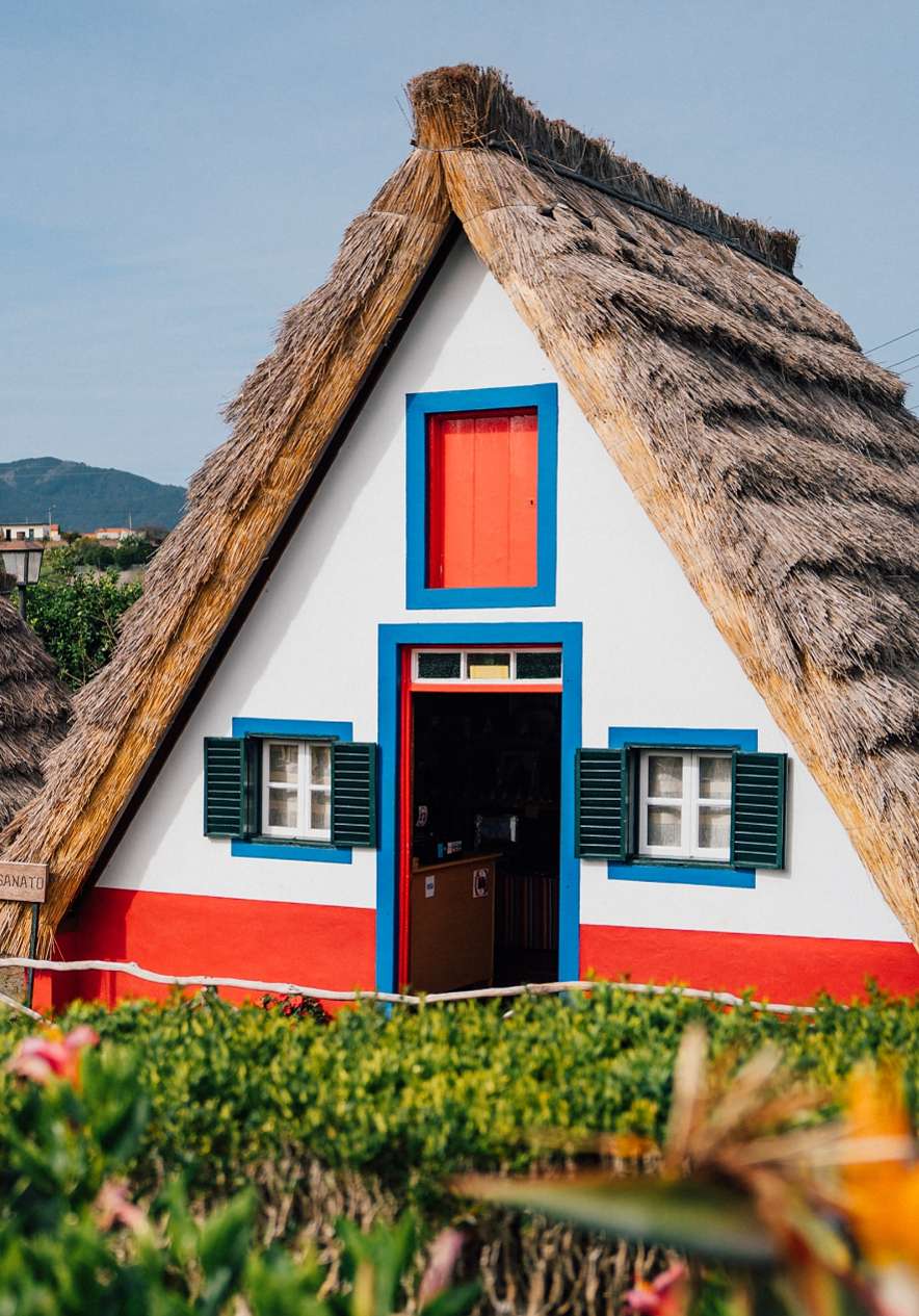 Casa tradicional com telhado de colmo, pintada de branco com detalhes em vermelho e azul, no Funchal
