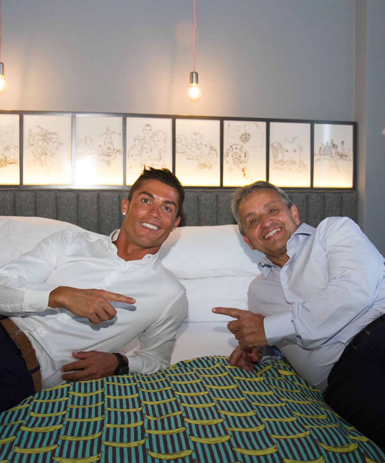 Het merk Pestana CR7 Lifestyle Hotels met twee glimlachende mannen op een bed onder warme hanglampen