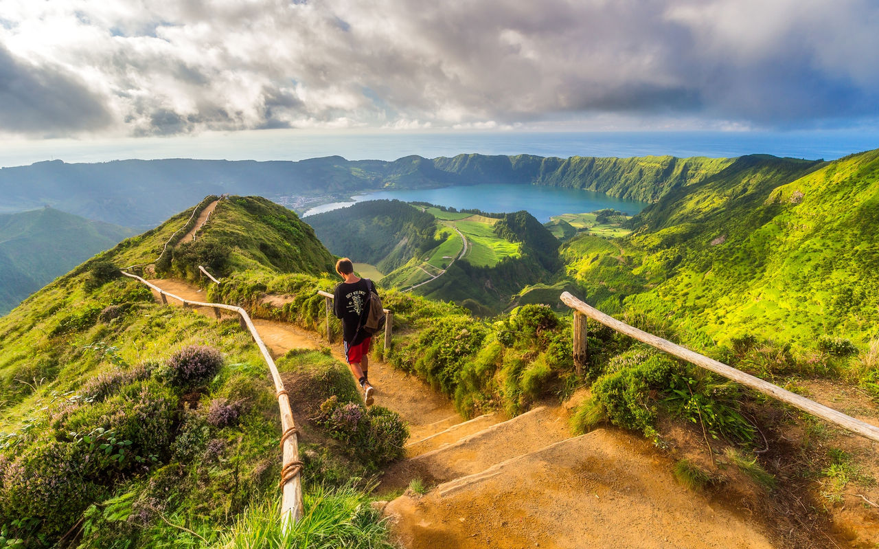 Homem caminha num trilho de terra com vista para a Lagoa das Sete Cidades, na Ilha de São Miguel, nos Açores