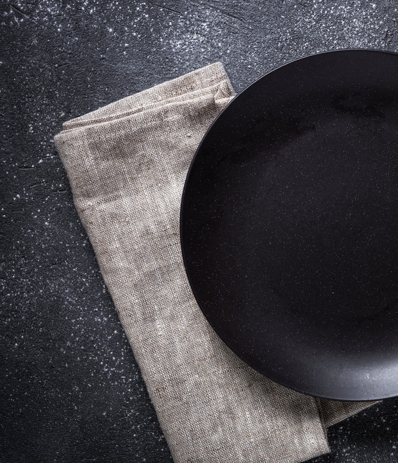 Gourmet dinner plate, matte black, placed on a light gray napkin, for a meal in Berlin