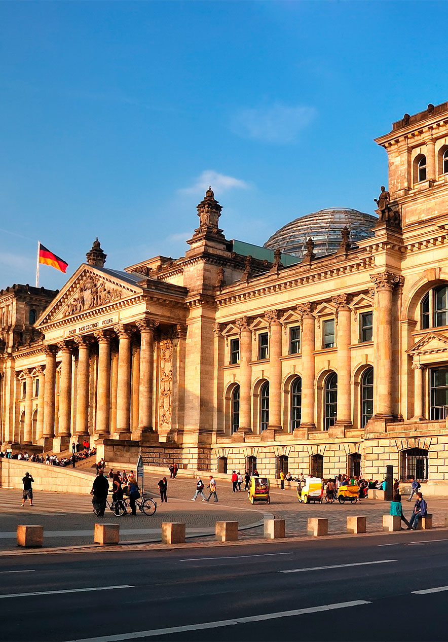 Reichstag building in Berlin at sunset with German flags raised and people walking in front