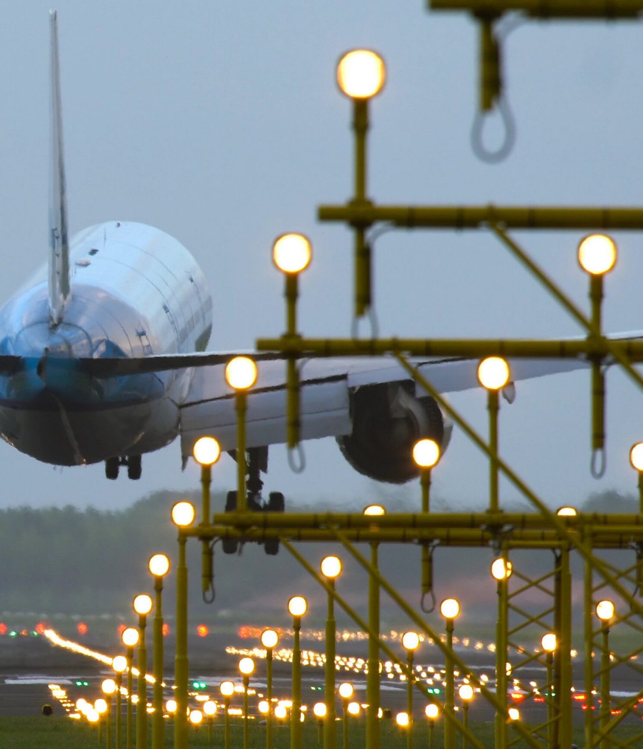 Explore Hotels in Amsterdam featuring a passenger jet descending above illuminated airport runway lights