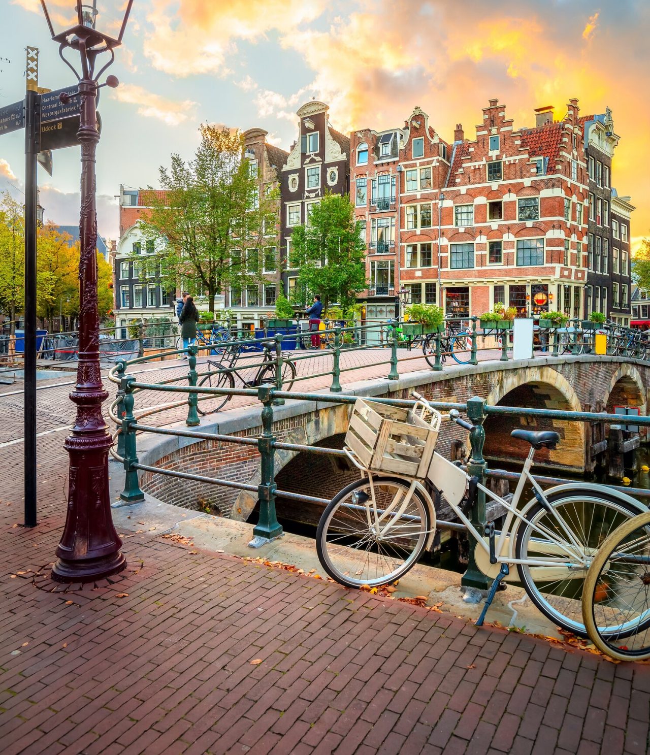 Explore Hotels in Amsterdam overlooking canal bridges lined with bicycles and historic brick houses at sunset
