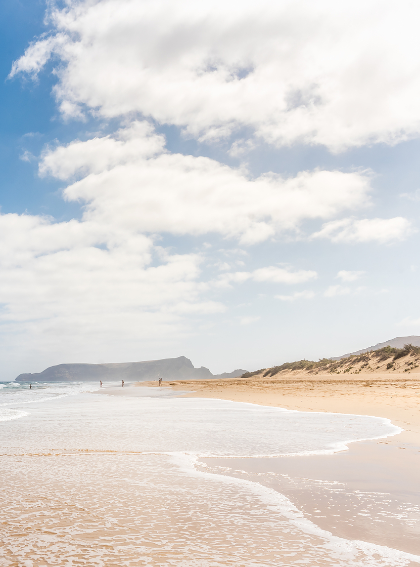 Long beach in Porto Santo with light sand, calm waves, and a blue sky with some clouds