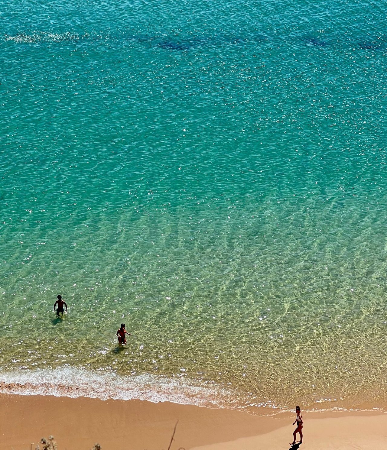 Aerial view of two people swimming at a beach with crystal-clear waters and golden sand, in the Algarve region