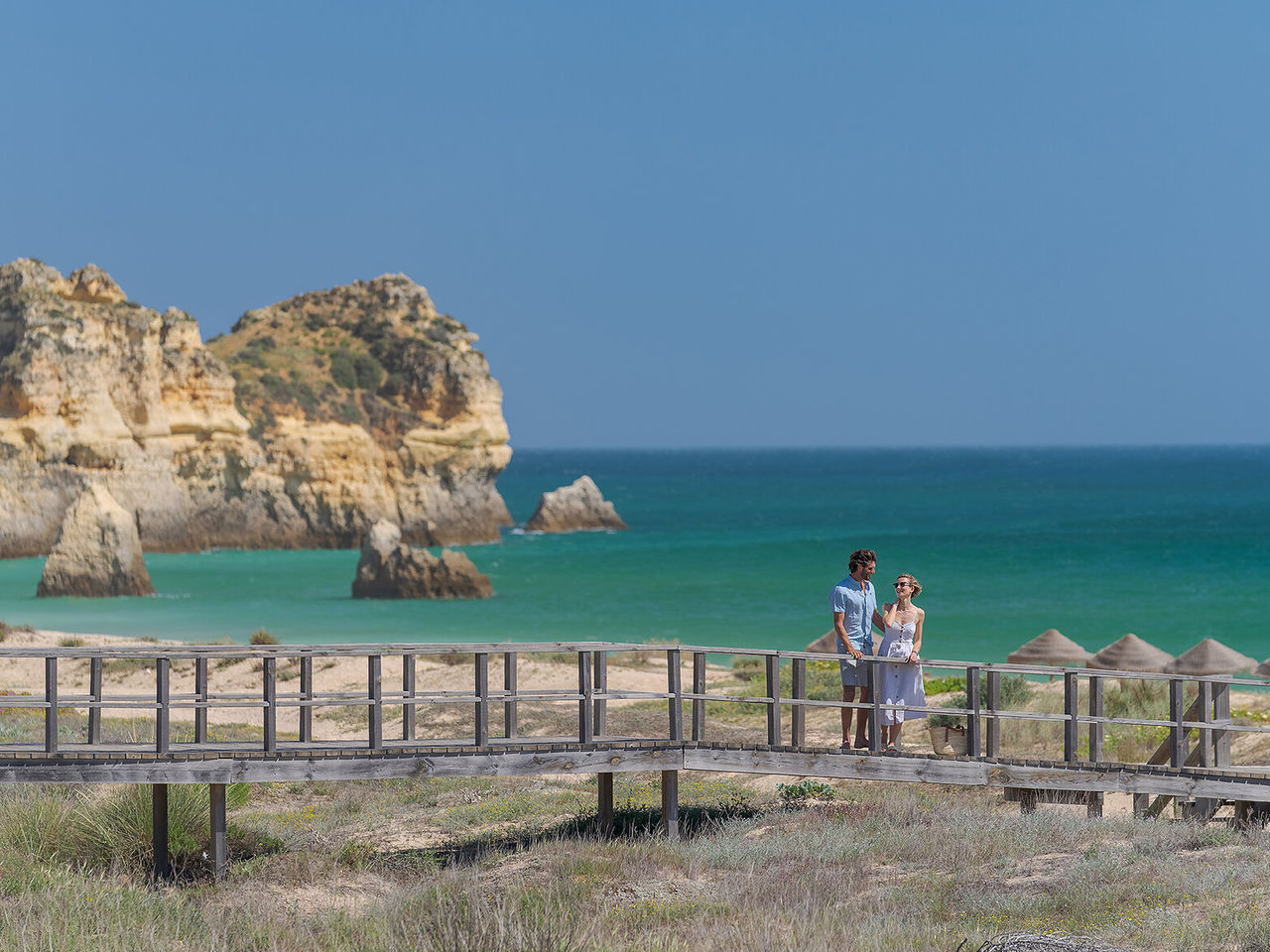 Couple admiring the view of a beach in Alvor, Algarve, while walking along the boardwalks by the sea