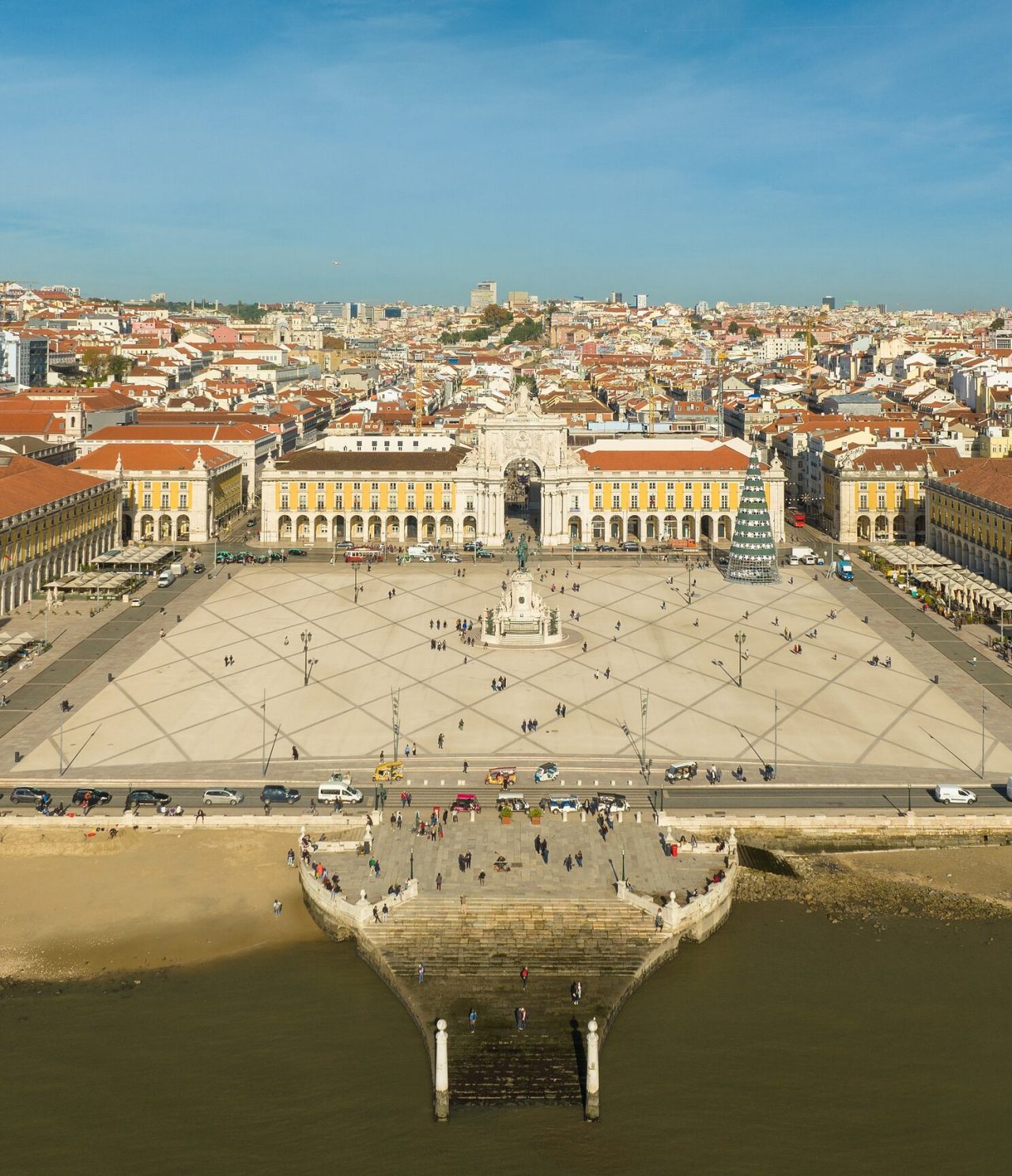 Aerial view of Praça do Comércio in Lisbon, with the Tagus River in front, statue in the middle, and a Christmas tree