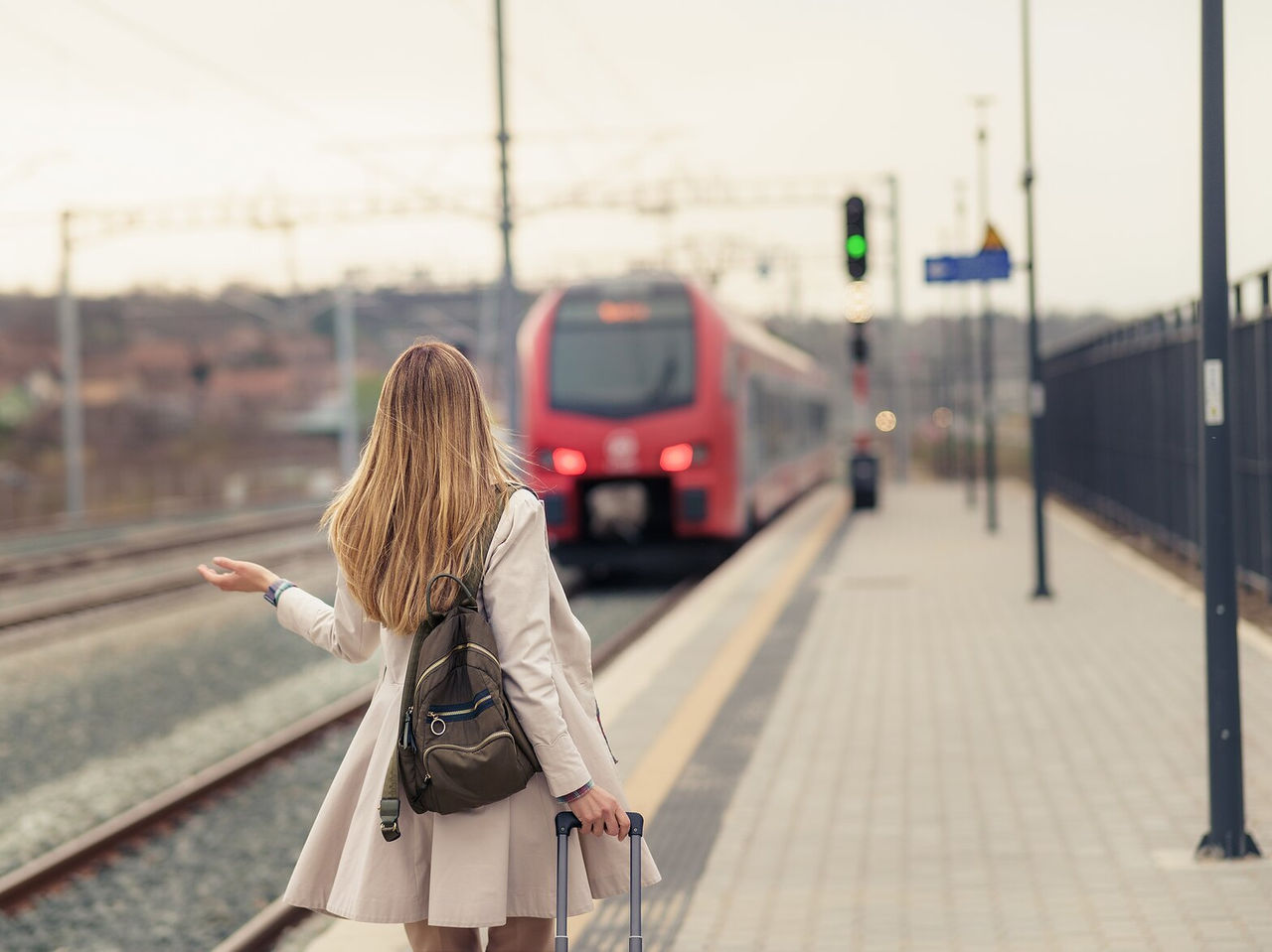 Explore Hotels in Lisbon where travellers wait beside a railway platform as a red train approaches at dusk