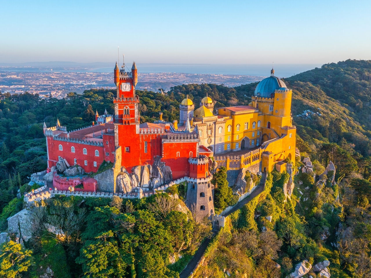 Explore Hotels in Lisbon featuring Pena Palace rising above forested hills with distant coastal views