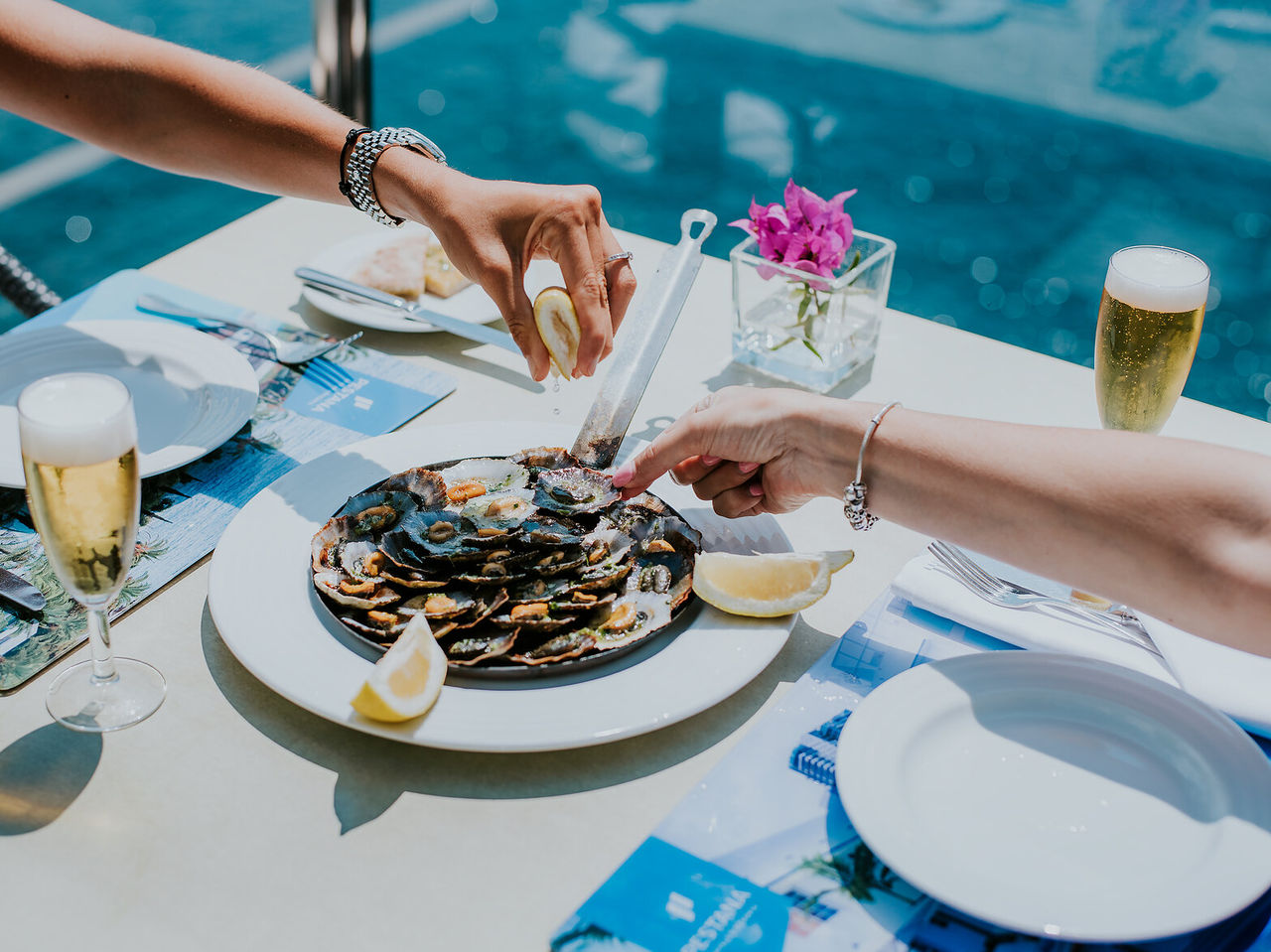 Dish with limpets being seasoned with lemon, accompanied by two glasses of beer