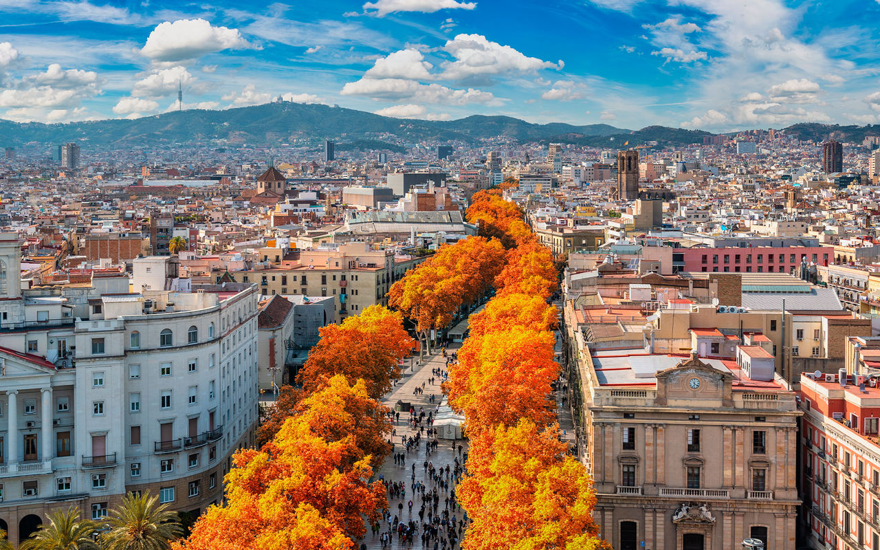 Aerial view over the city of Barcelona, with people strolling, colorful autumn trees, and various buildings