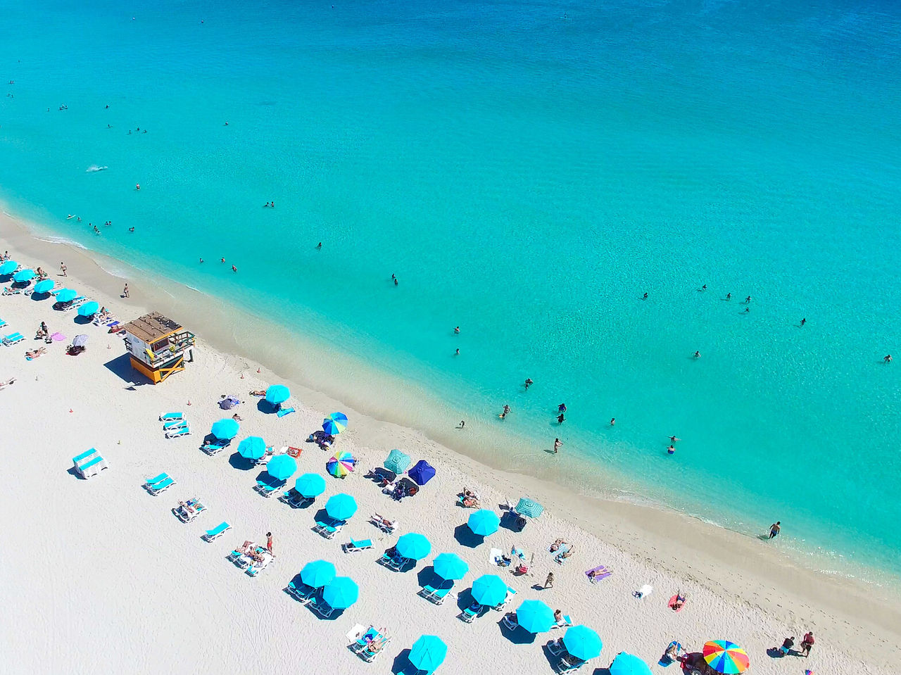 Miami Beach, Florida, with white sand, turquoise seawater, and people swimming and sunbathing on chairs