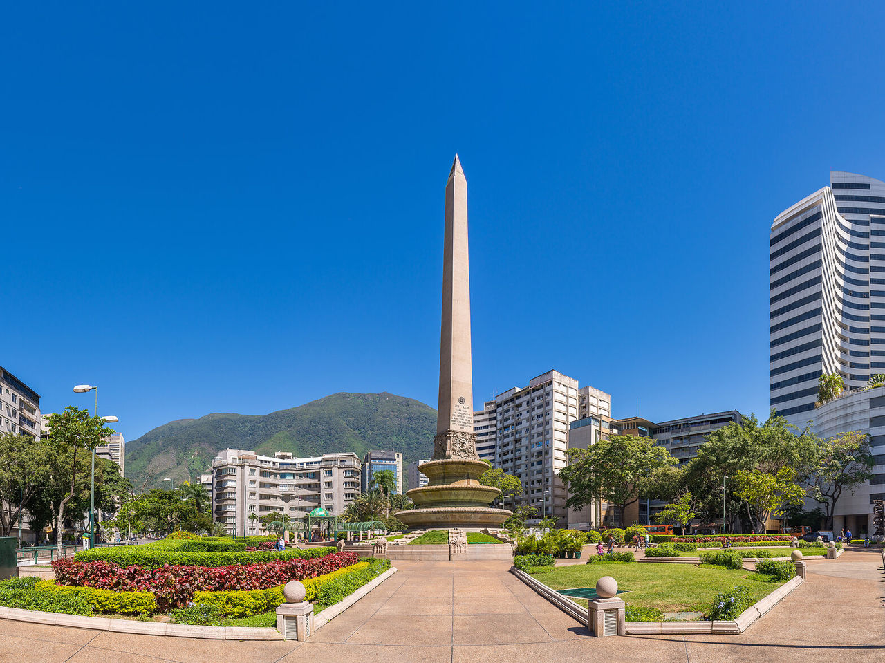 Obelisk Monument, large stone column in the middle of a park with flowers, surrounded by tall buildings in Caracas