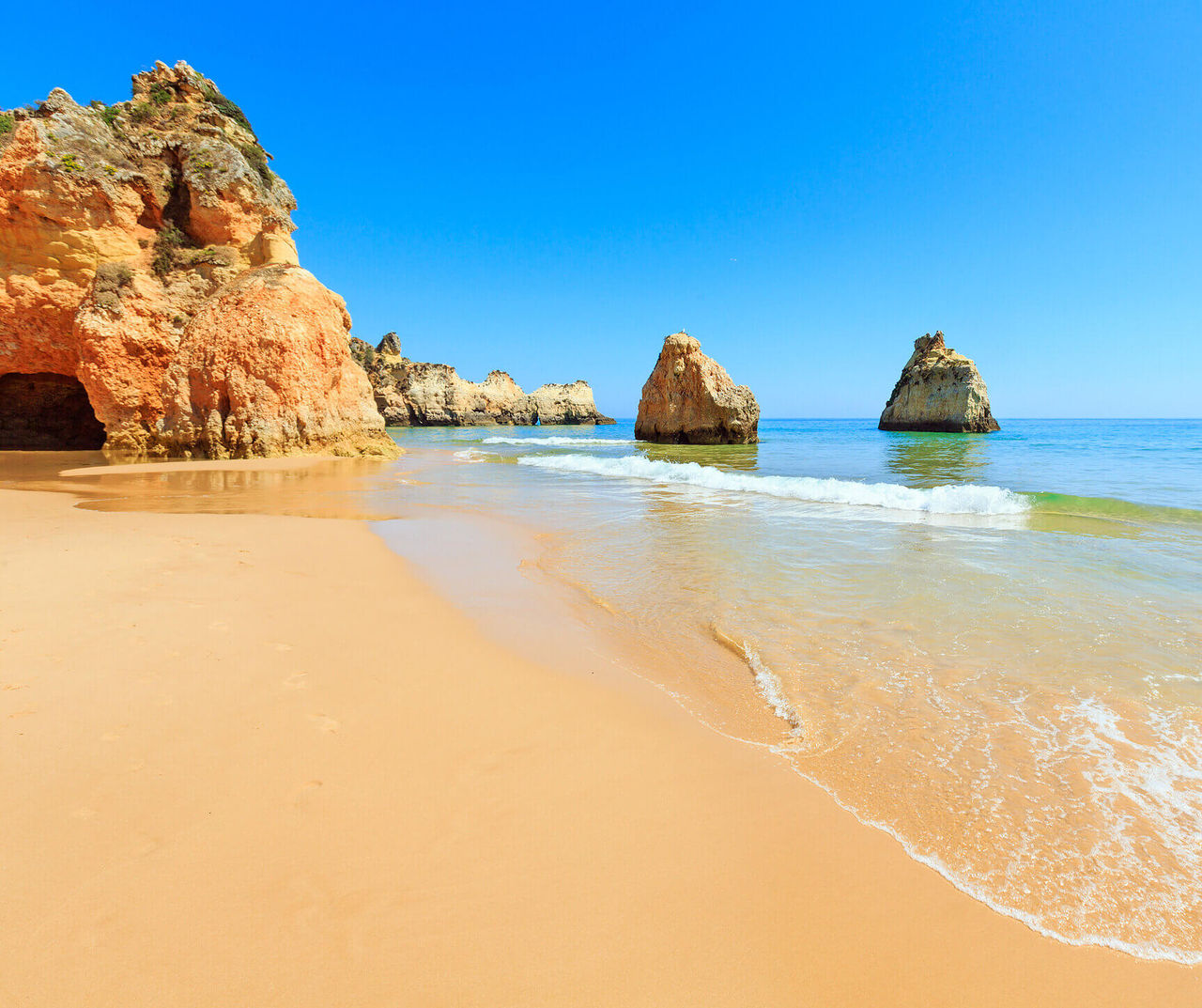 Sunny Algarve beach near cliffs and sea stacks with gentle waves along the shore for Pestana Hotel Group