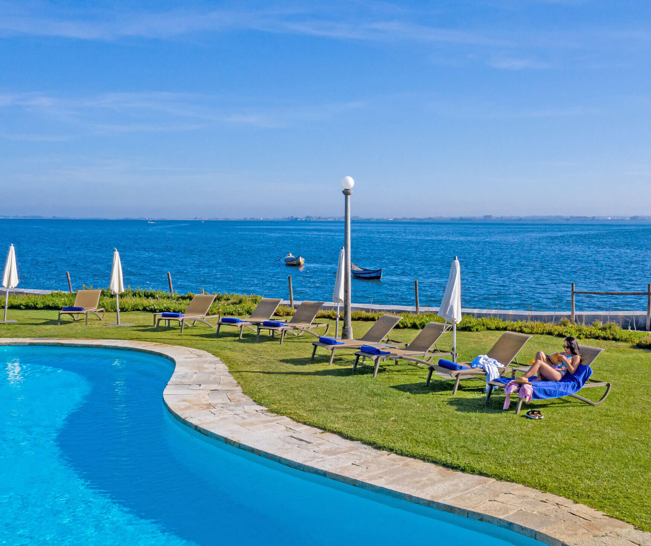 center-portugal hotel overlooking a curved pool, sun loungers on the lawn and calm blue water beyond