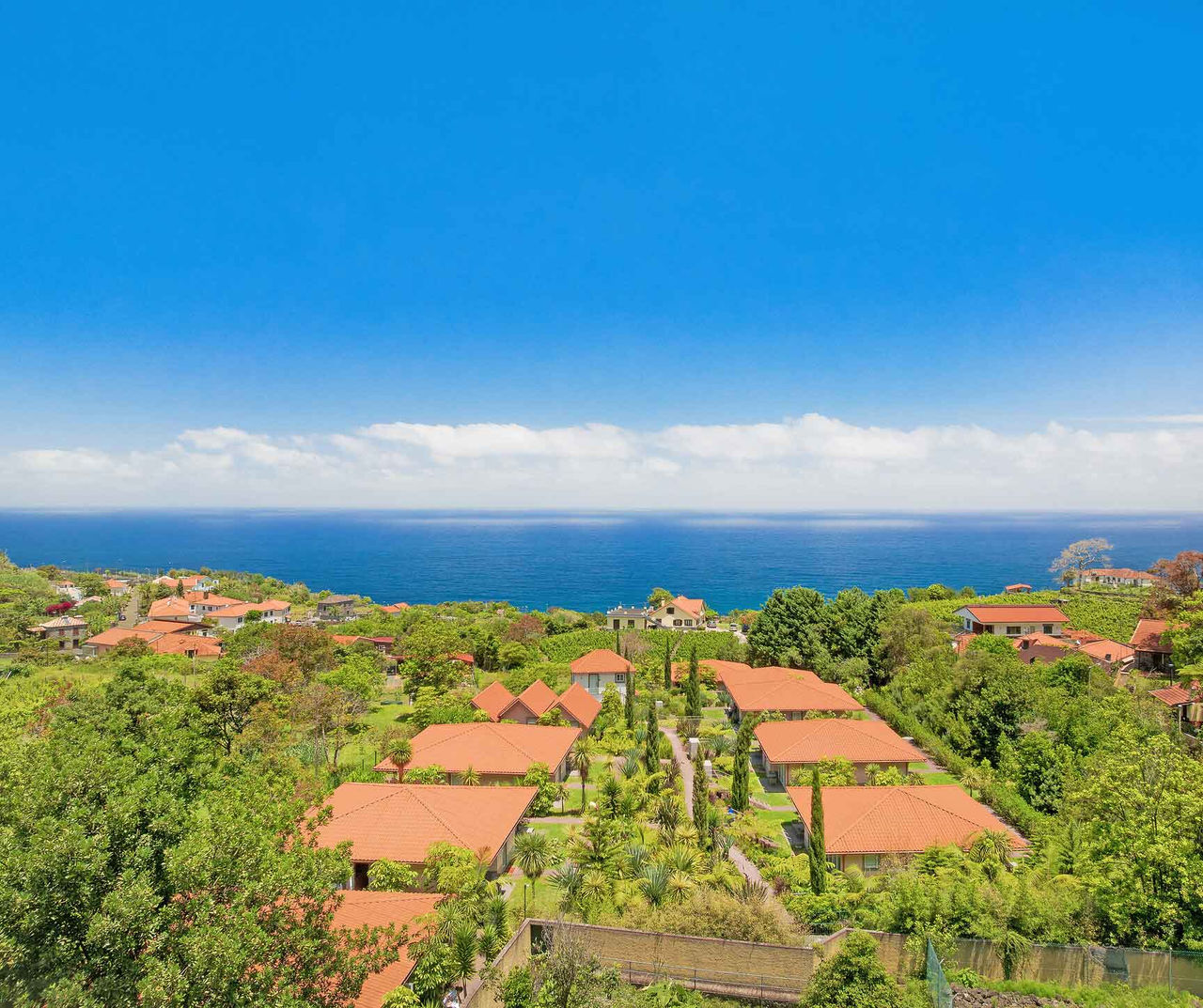 Madeira hotel overlooking terracotta roof villas surrounded by gardens beside the Atlantic coast under clear skies