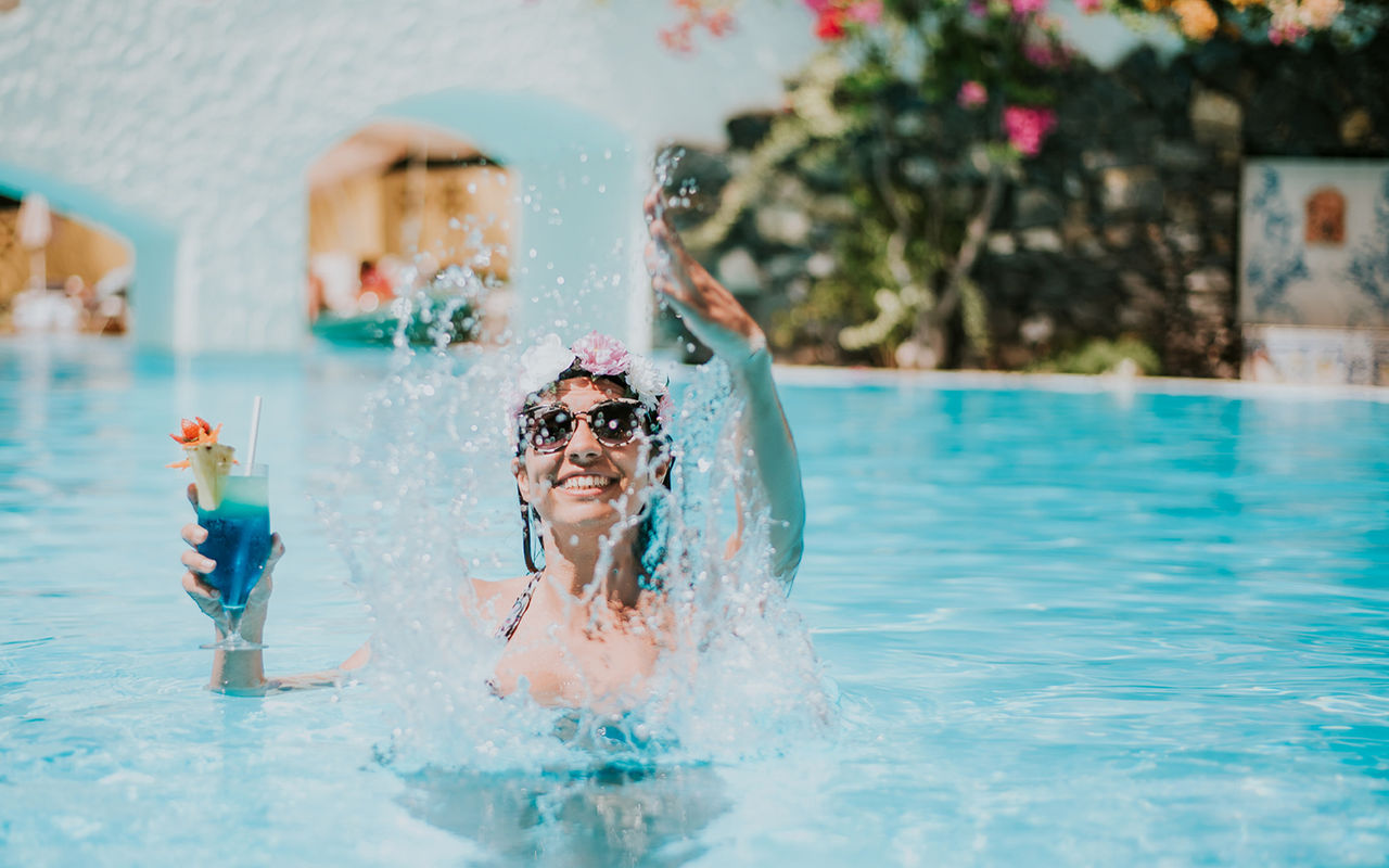 Happy woman playing with water, holding a cocktail, enjoying the all-inclusive package without worries